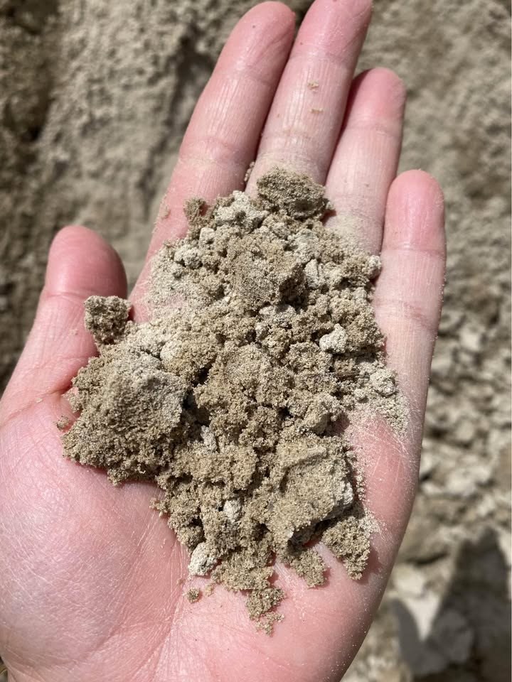 A hand holding crusher fines, fine grey grit that packs down smooth underfoot, what Utah sells in place of decomposed granite