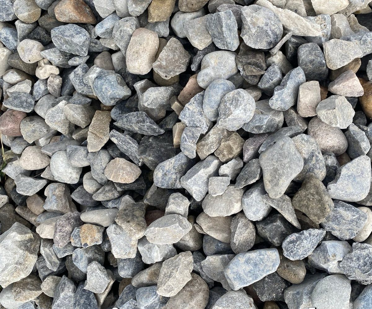 A close bed of angular grey drain rock in a range of sizes, filling the frame