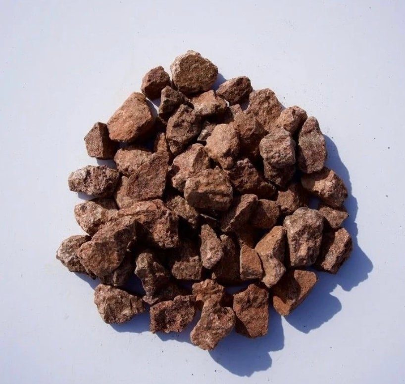 A pile of rust-red lava rock, porous and light, on a white background