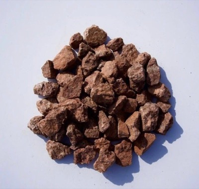 A pile of rust-red lava rock, porous and light, on a white background