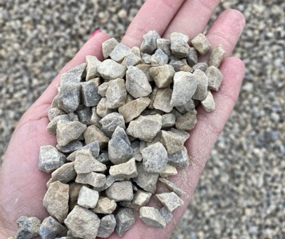 A hand holding tank bedding, small uniform pale grey stone of an even size